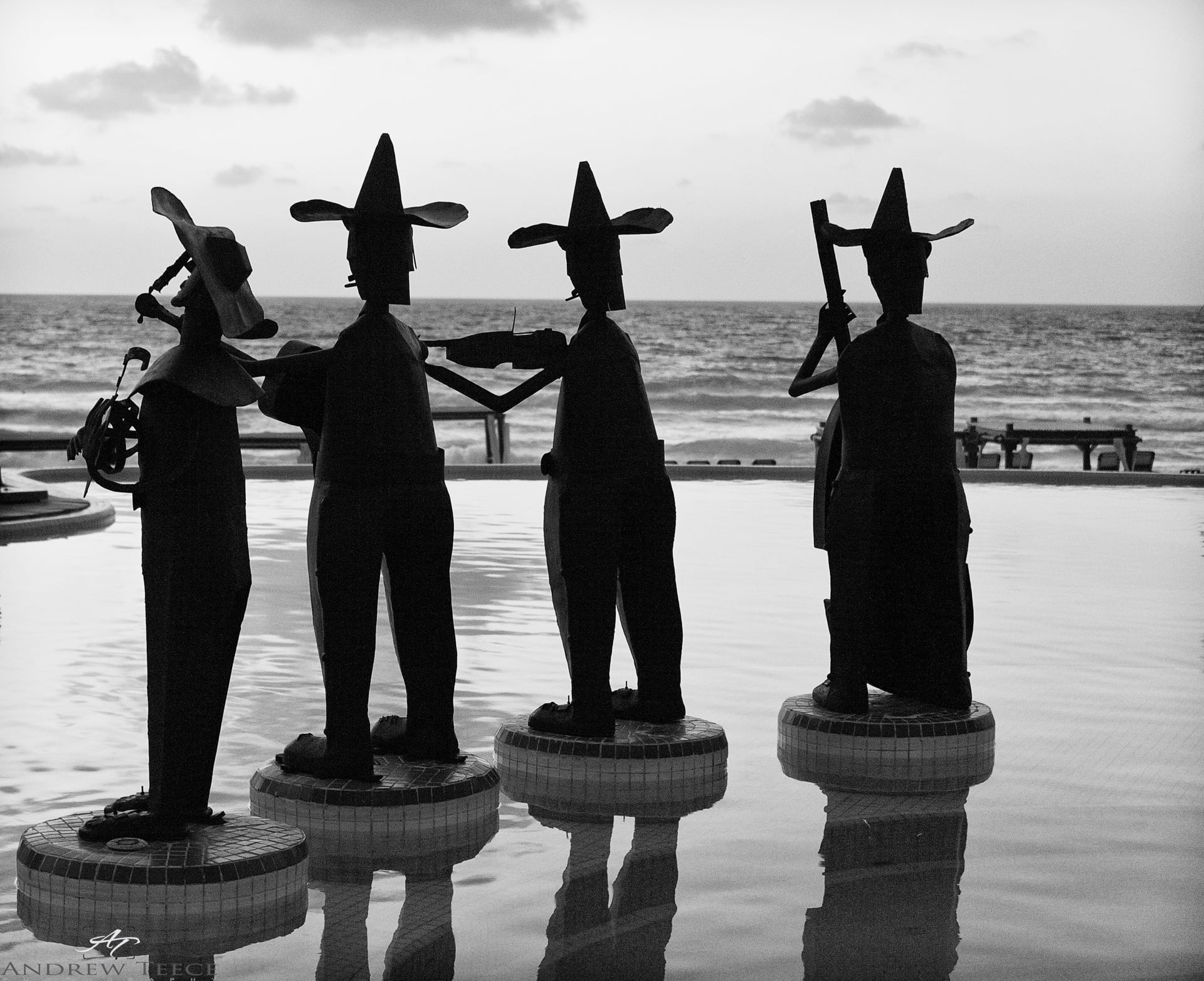 Four metal musician statues silhouetted against the sea at dusk